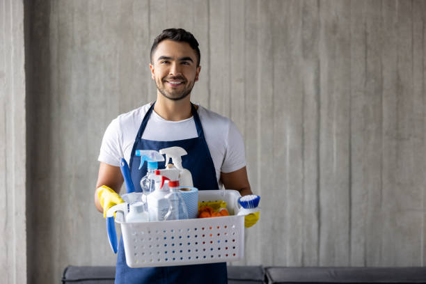 A happy professional cleaner holding a basket of cleaning products and smiling at the camera.